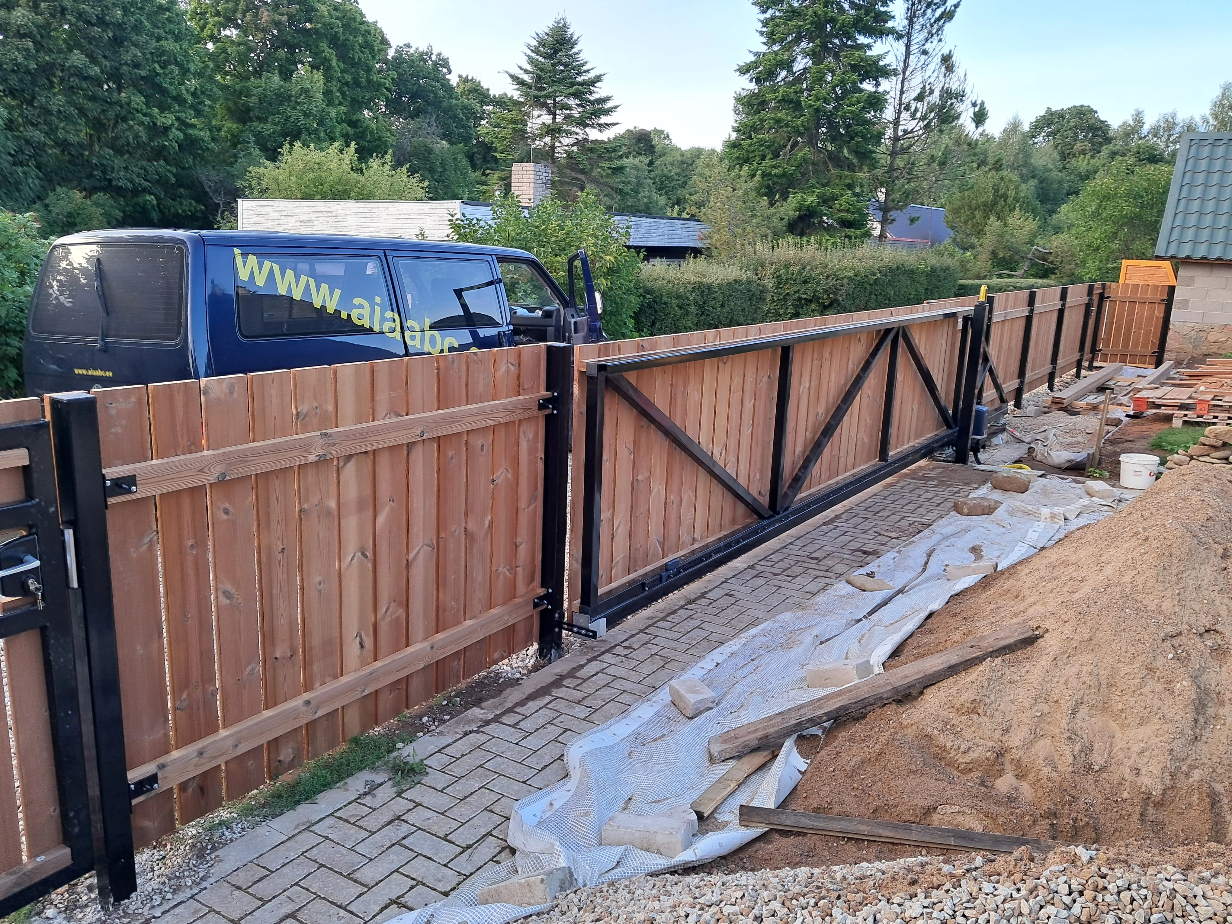 Varav - pruun puitlaudis liugvärav mustade metalpostide vahel paigaldamisel