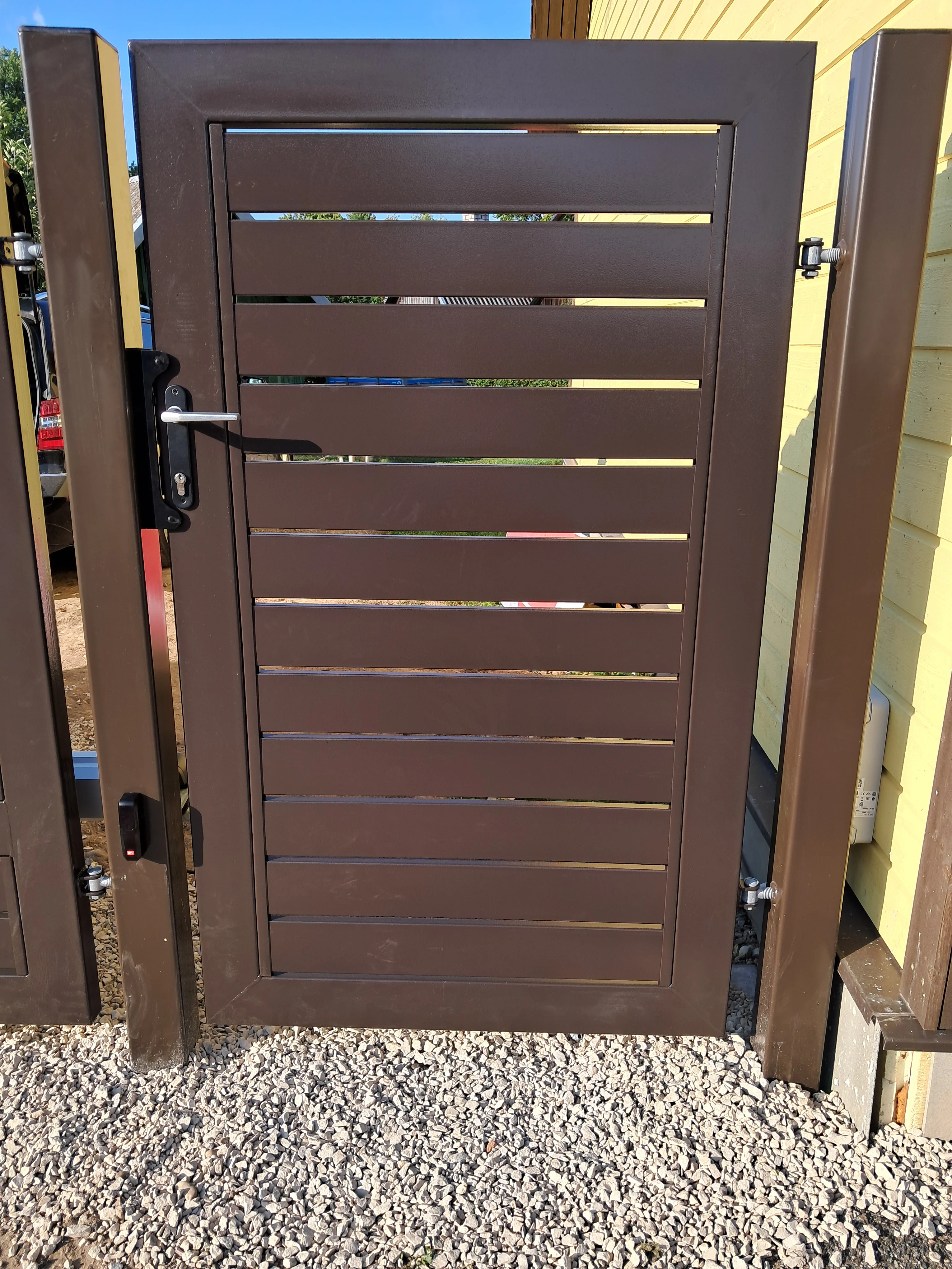 Varav - metallist jalakäijavärav horisontaalsete lippidega kivi seina kõrval